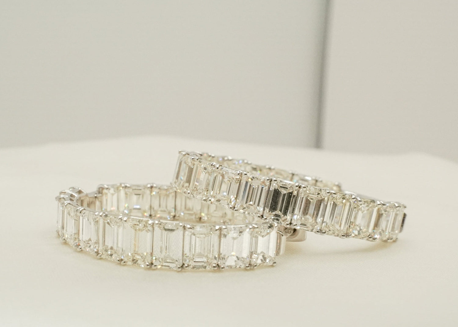 Two silver diamond hoop earrings on a white surface with a neutral background