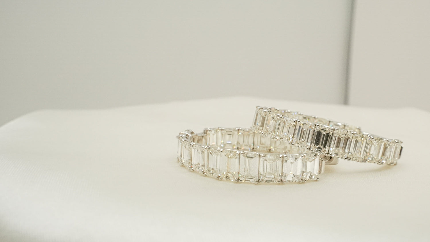 Two white gold diamond hoop earrings on a white surface with a neutral background