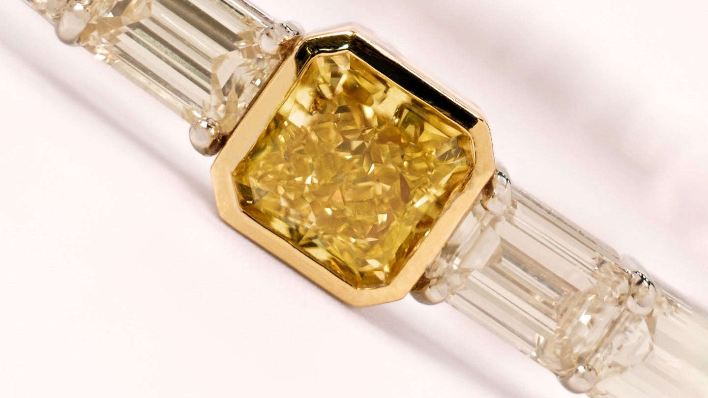 Close up of a bracelet with a yellow diamond and white baguette-cut diamonds on a white background
