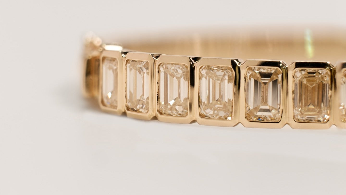 Close up of gold bracelet with emerald-cut diamonds on a light background