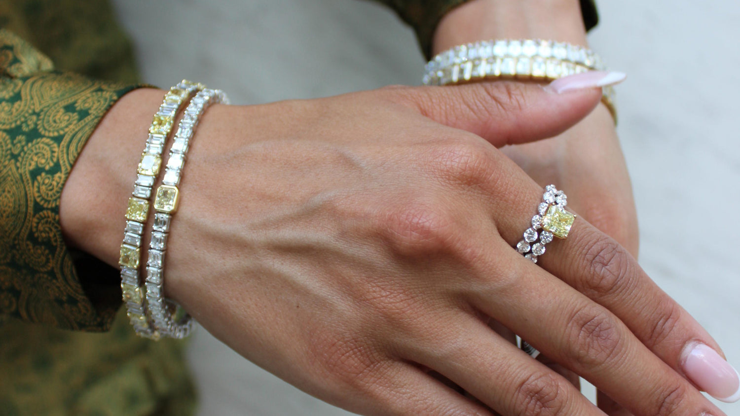Close-up of hands wearing multiple diamond bracelets and rings on a plain background